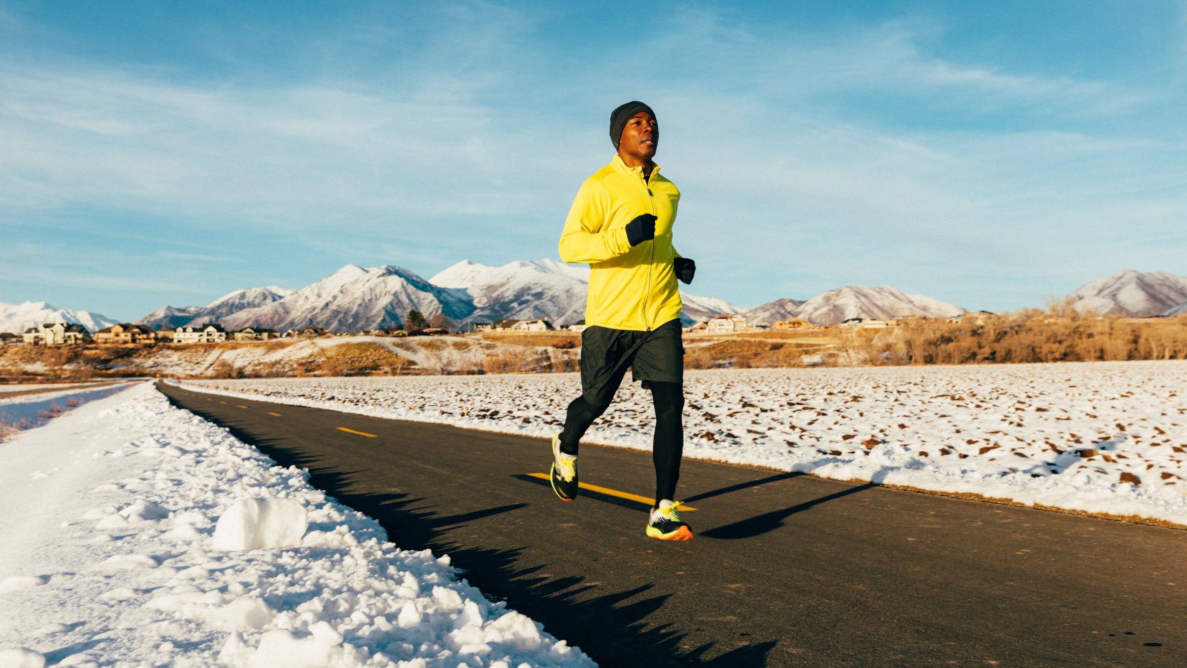 man running on a road in winter in front of snowy mountains